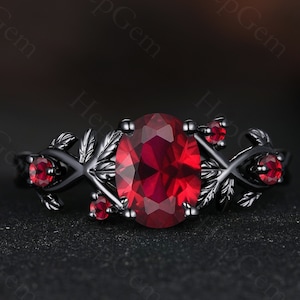 May include: A black ring with a large red oval gemstone surrounded by smaller red gemstones. The ring features a delicate vine design with leaves.
