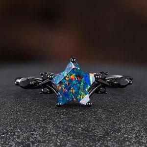 May include: A black ring with a star-shaped opal gemstone. The ring has a delicate, twisted band with black accents.
