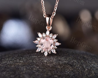 May include: A delicate rose gold necklace with a round pink gemstone surrounded by smaller clear gemstones in a sunburst design.