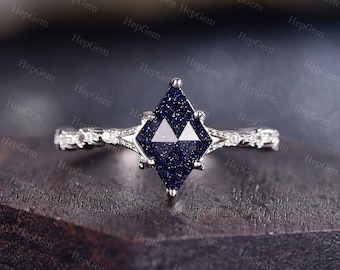May include: A silver ring with a blue gemstone in a square shape. The gemstone is set in a prong setting and has a sparkly finish. The band of the ring is decorated with small diamonds.