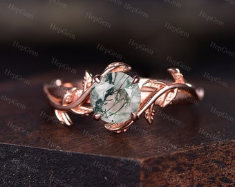 Puede incluir: Un anillo de oro rosa con una piedra preciosa de ágata verde musgo engastada en un delicado diseño de hojas.