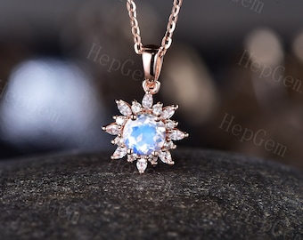 May include: A rose gold necklace with a moonstone pendant surrounded by a halo of smaller clear stones. The pendant is shaped like a flower.