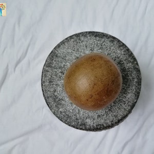 May include: A brown, round object sits in the center of a gray, speckled mortar and pestle. The mortar and pestle are made of stone.