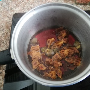 May include: A stainless steel pot with a black handle sits on a black electric stovetop. The pot contains a red liquid with brown pieces of fruit and spices.
