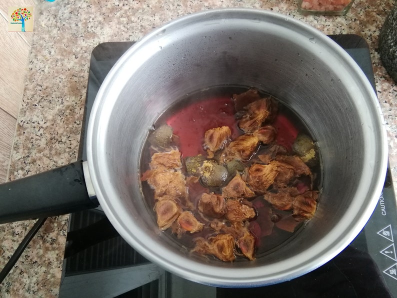 May include: A stainless steel pot with a black handle sits on a black electric stovetop. The pot contains a red liquid with brown pieces of fruit and spices.