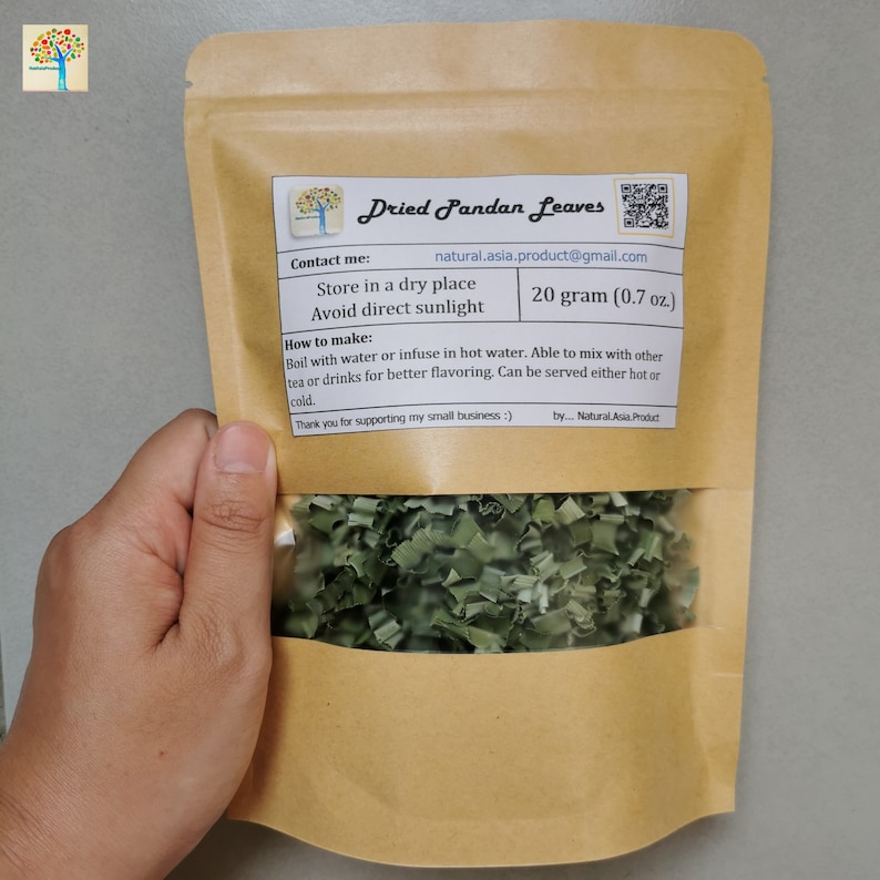 Pu&ograve; includere: Un sacchetto di carta marrone con una finestra trasparente che mostra foglie di pandan essiccate verdi. Il sacchetto ha un'etichetta con il testo "Dried Pandan Leaves", "Contact me: natural.asia.product@gmail.com", "Store in a dry place", "Avoid direct sunlight", "20 grammi (0,7 oz)", "How to make: Boil with water or infuse in hot water. Able to mix with other tea or drinks for better flavoring. Can be served either hot or cold. Thank you for supporting my small business :) by... Natural Asia Product".