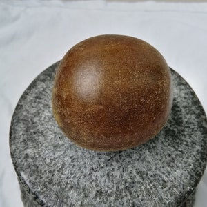 May include: A large, round, brown fruit with a rough texture sits on a gray, textured surface.