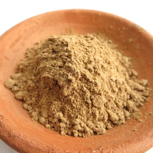 Puede incluir: Primer plano de un pequeño plato de terracota lleno de un polvo marrón claro. El polvo está finamente molido y tiene una textura ligeramente rugosa.