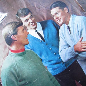 May include: Vintage knitting book cover featuring three men wearing knitted sweaters and cardigans in shades of blue and green. The cover has the text "Fontana Knitting Book" in a retro font. The image has a vintage aesthetic.