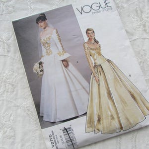 Puede incluir: Patrón de costura original de novia Vogue con ilustraciones de dos vestidos de novia. Uno es blanco con bordados dorados, el otro es color champán con bordados dorados. El patrón está sobre un fondo blanco.