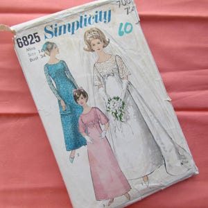 May include: A vintage Simplicity sewing pattern, number 6825, showing illustrations of three women in dresses. The pattern is size 14, bust 34. The cover is aged, set against a pink backdrop.
