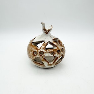 Könnte beinhalten: Ein weißer Kerzenhalter aus Keramik in Form eines Granatapfels mit brauner Glasur und filigranen Ausschnitten.