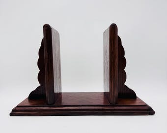 May include: A dark brown wooden bookend set. The bookends have a rectangular base and two upright supports with a scalloped edge design. The wood grain is visible, and the finish is glossy.