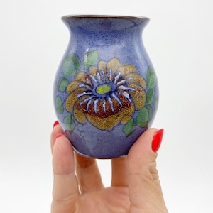 May include: A small, blue ceramic vase with a hand-painted floral design. The vase features a large yellow flower with a green center and brown accents.