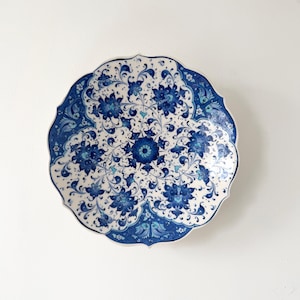 May include: A ceramic plate with a scalloped edge, decorated with a blue floral pattern on a white background. The design features detailed flowers and scrollwork, creating a classic and elegant aesthetic. The plate is suitable for decorative purposes.