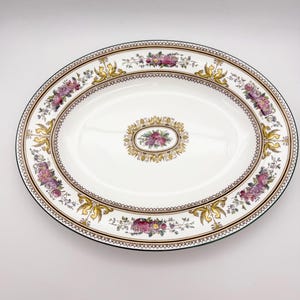 May include: Oval serving platter with a white background. The platter features a floral design with pink and purple flowers, gold accents, and a brown border. The rim is green.