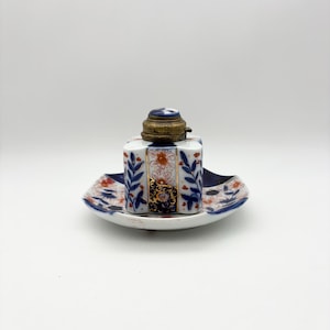 May include: Antique inkwell set with a hexagonal ink bottle and a matching dish. The ink bottle has a brass lid and is decorated with blue floral and leaf patterns, along with orange and gold accents. The dish has a similar design.