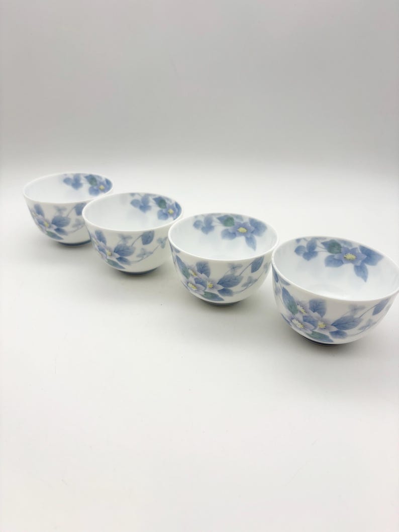 K&ouml;nnte beinhalten: Vier wei&szlig;e Keramikschalen mit blauem Blumenmuster. Die Schalen sind in einer Reihe angeordnet und zeigen jeweils ein zartes Design aus blauen Blumen und gr&uuml;nen Bl&auml;ttern. Ideal zum Servieren kleiner Portionen.