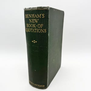 Könnte beinhalten: Ein grünes Hardcover-Buch mit dem Titel "Benham's New Book of Quotations" in goldener Schrift. Das Buch ist geschlossen und steht aufrecht auf einer weißen Oberfläche.