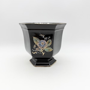 May include: Black, octagonal ceramic planter with a floral design. The planter has a glossy finish and a raised base. The floral design includes blue, gold, and green accents. Suitable for indoor or outdoor use.