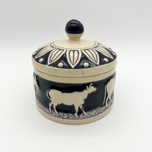 May include: A white ceramic butter dish with a blue and white floral design on the lid and a blue band around the bottom with white cows in relief.