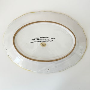 Pu&ograve; includere: Piatto da portata ovale in ceramica bianca con bordo giallo e un'iscrizione manoscritta sul fondo: "GUIDO BARBIERI, SAN LORENZELLO - OM - ITALIA, WWW.CERAMICABARBIERI, IT". &Egrave; visibile anche un piccolo adesivo rotondo con il testo "DE SANCHIS".