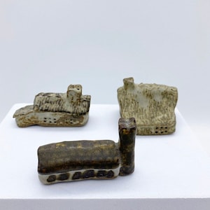 Può includere: Tre piccole case in ceramica in varie tonalità di marrone e bianco. Le case sono realizzate a mano e hanno una finitura rustica e testurizzata.
