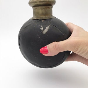 May include: A black leather bottle with a silver top. The bottle is round and has a small opening at the top.
