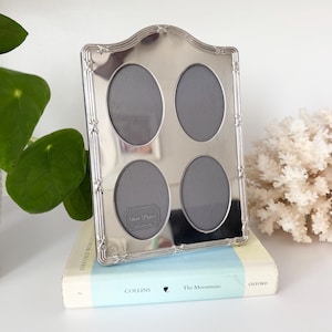 May include: A silver-plated multi-photo frame with a polished finish and a decorative arched top. The frame features four oval-shaped openings for photographs and includes a small rectangular plaque with the text Silver Plated Made in England.