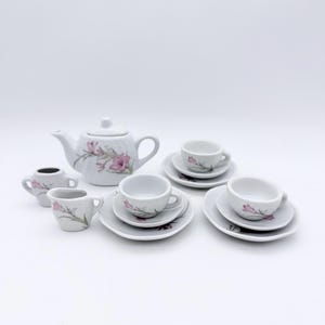 Puede incluir: Un juego de té en miniatura de porcelana blanca con detalles florales rosas. El juego incluye una tetera, una lechera, un azucarero y varias tazas con platillos. Diseñado para el juego de niños o fines decorativos.