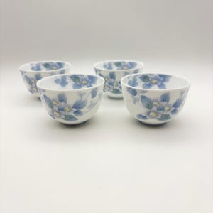 K&ouml;nnte beinhalten: Vier wei&szlig;e Keramikschalen mit einem Blumendesign mit blauen und gelben Blumen und gr&uuml;nen Bl&auml;ttern. Die Schalen sind auf wei&szlig;em Hintergrund angeordnet. Das Blumenmuster wiederholt sich auf jeder Schale.