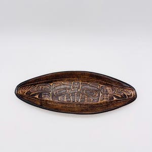 May include: A wooden serving tray with a carved design of a stylised animal. The tray is dark brown and has a glossy finish.