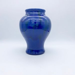 May include: A cobalt blue ceramic vase with a rounded body and a flared neck. The vase has a glossy finish and subtle variations in the blue color.