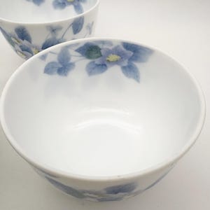 K&ouml;nnte beinhalten: Zwei wei&szlig;e Keramikschalen mit floralem Design. Die Schalen haben ein zartes Muster aus blauen Blumen und Bl&auml;ttern am Rand. Die Blumen haben gelbe Zentren. Die Schalen sind leer und scheinen neu zu sein.