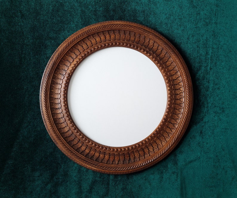 May include: A round, wooden picture frame with a carved design. The frame is brown and has a white background.