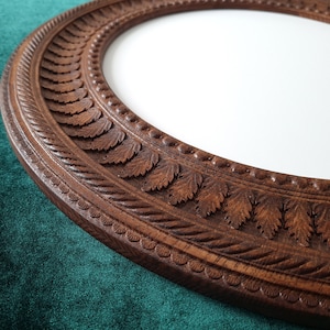 May include: A dark brown wooden oval picture frame with a carved leaf design. The frame is on a green velvet surface.