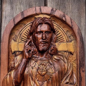 Op de afbeelding: Een houten beeldhouwwerk van Jezus Christus met een gouden hart en een kruis erachter. Het beeldhouwwerk is op een houten achtergrond.