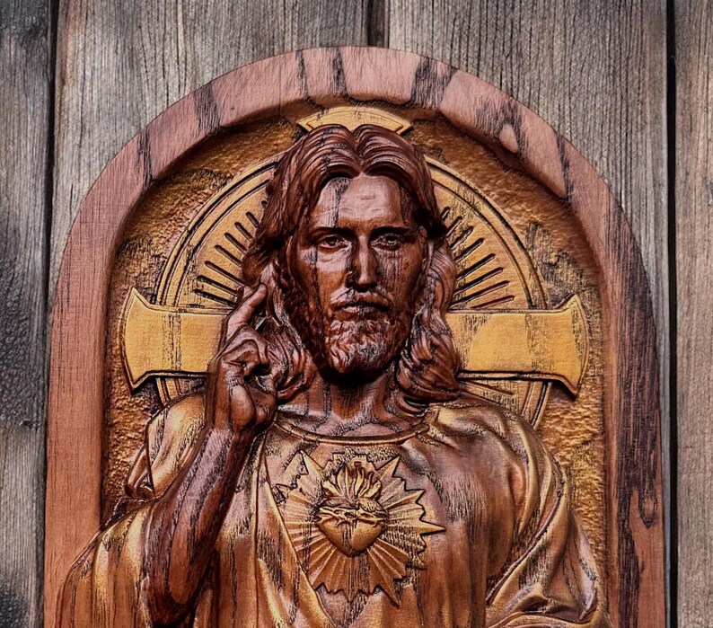 Op de afbeelding: Een houten beeldhouwwerk van Jezus Christus met een gouden hart en een kruis erachter. Het beeldhouwwerk is op een houten achtergrond.