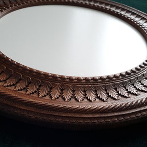 May include: A round, wooden mirror with a detailed, carved frame. The frame features a rope-like design and a row of leaves around the edge.