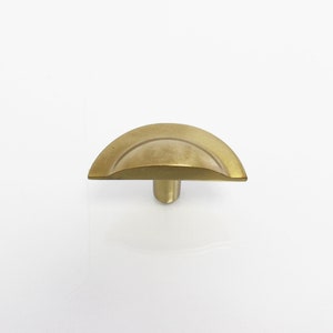 Może przedstawiać: Złoty, półokrągły gałka do szafki z gładką, zaokrągloną powierzchnią i cylindryczną podstawą.