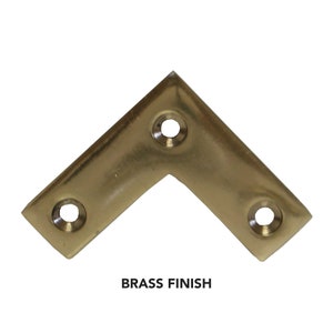May include: Brass corner brace with four screw holes.  The brace is a light gold color.  BRASS FINISH is written below the brace.
