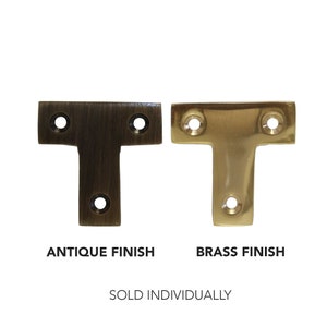 May include: Two T-shaped metal brackets, one in antique brass finish and one in polished brass finish.  The brackets are sold individually.  "Sold Individually" text is below the brackets.