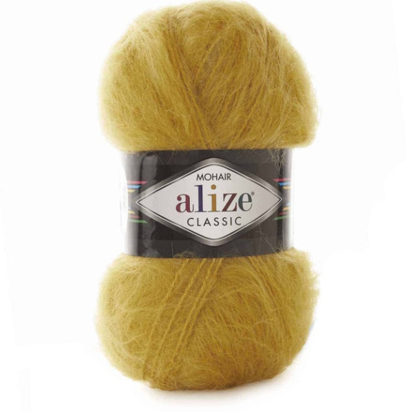 May include: A ball of Alize Classic mohair yarn in a golden yellow hue. The yarn is wrapped with a black label featuring the brand name and logo. The yarn appears soft and fluffy, ideal for knitting or crocheting projects.
