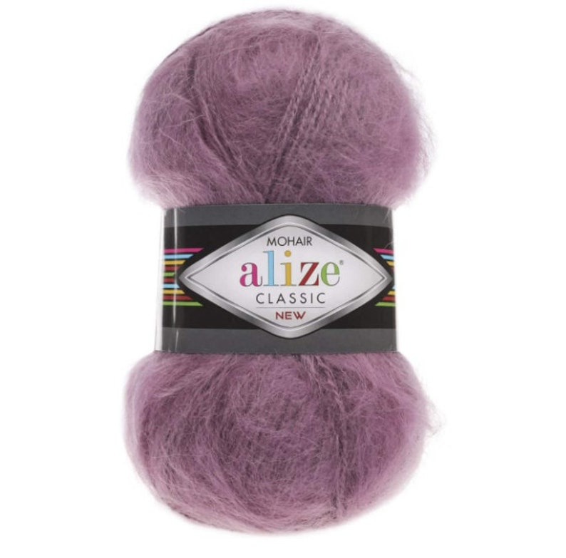 May include: A ball of lavender mohair yarn with a black and silver label. The label reads "MOHAIR alize CLASSIC NEW" in white and green text. The yarn is fluffy and soft, ideal for knitting or crocheting projects.