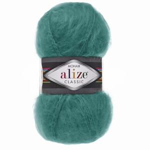 May include: A ball of teal mohair yarn with a label that reads "MOHAIR ALIZE CLASSIC". The yarn is fluffy and soft, ideal for knitting or crocheting projects. The label has a black background with colorful stripes.