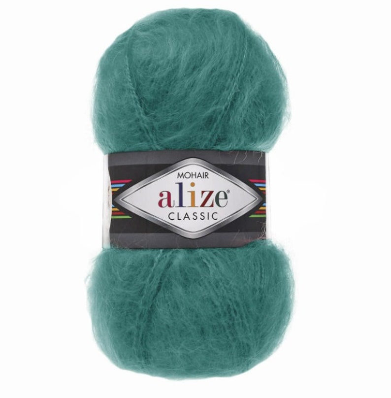 May include: A ball of teal mohair yarn with a label that reads "MOHAIR ALIZE CLASSIC". The yarn is fluffy and soft, ideal for knitting or crocheting projects. The label has a black background with colorful stripes.