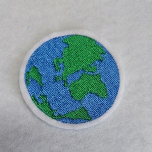 Könnte beinhalten: Ein gestickter Aufnäher der Erde in Blau und Grün. Der Aufnäher ist rund und hat einen weißen Rand.