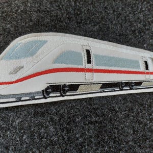 Könnte beinhalten: Weißer und roter gestickter Aufnäher eines Hochgeschwindigkeitszugs mit schwarzen Rädern.