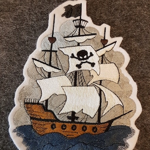 Könnte beinhalten: Gestickter Aufnäher eines Piratenschiffs, das auf blauen Wellen segelt. Das Schiff hat ein weißes Segel mit einem schwarzen Totenkopf und Knochen. Das Schiff ist braun mit weißen Akzenten.