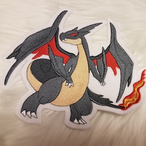 Könnte beinhalten: Gestickter Aufnäher eines schwarzen und roten Drachen mit gelben Flammen. Der Drache hat einen großen, spitzen Kopf mit einem roten Kamm und einen langen, dünnen Schwanz.